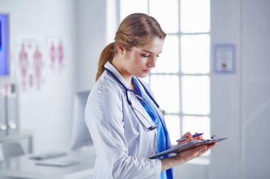 Genç kadın doktor hastane ofisinde gülümseyen pano ile kurulu ile duruyor