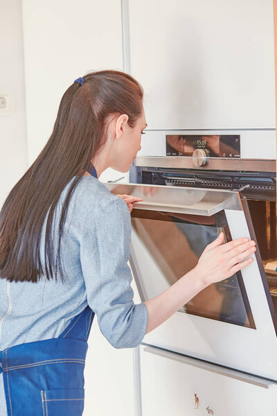Beautiful woman in the kitchen, waiting with the front of the oven