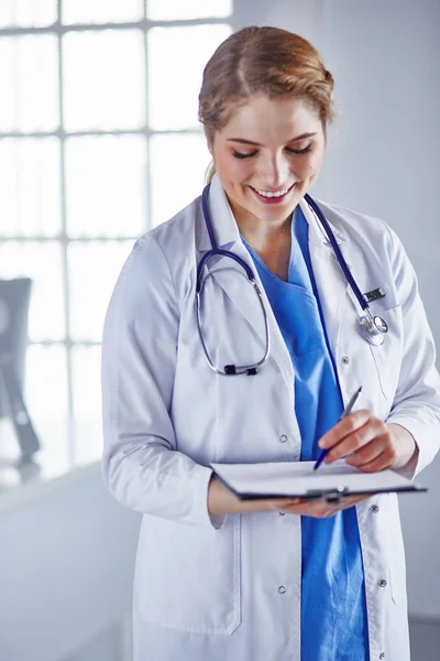 Giovane donna medico è in piedi con bordo con appunti sorridente in ufficio ospedaliero — Foto Stock