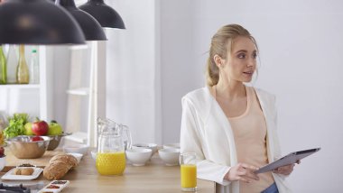 Mutfakta dijital tablet kullanan güzel genç bir kadın.