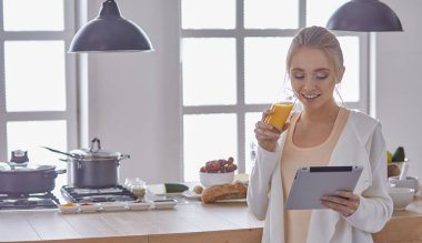 Mutfakta dijital tablet kullanan güzel genç bir kadın.