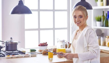 Mutfakta dijital tablet kullanan güzel genç bir kadın.