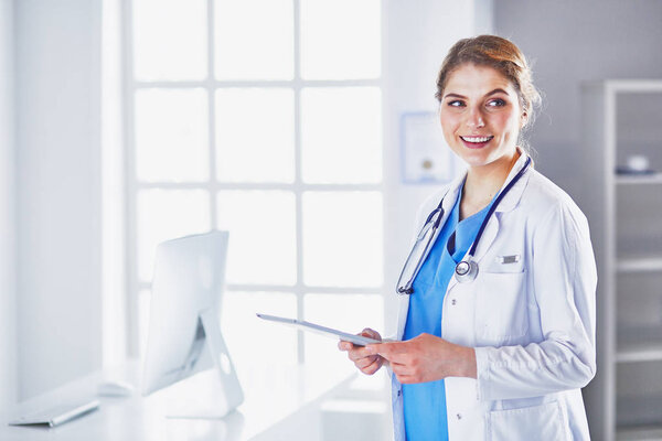 Young woman doctor is standing with board with clipboard smilin