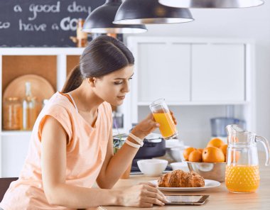 Cep telefonu görünümlü ve cam portakal suyu bir mutfakta Kahvaltı yaparken tutan gülümseyen güzel kadın