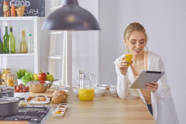 Mutfakta dijital tablet kullanan güzel genç bir kadın.