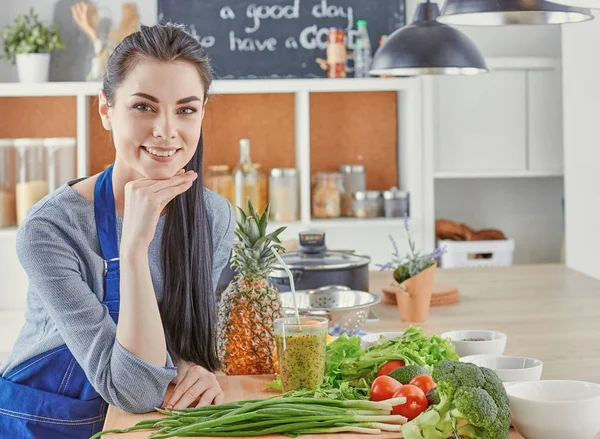 Happy young woman in kitchen with fresh vegetables on the table