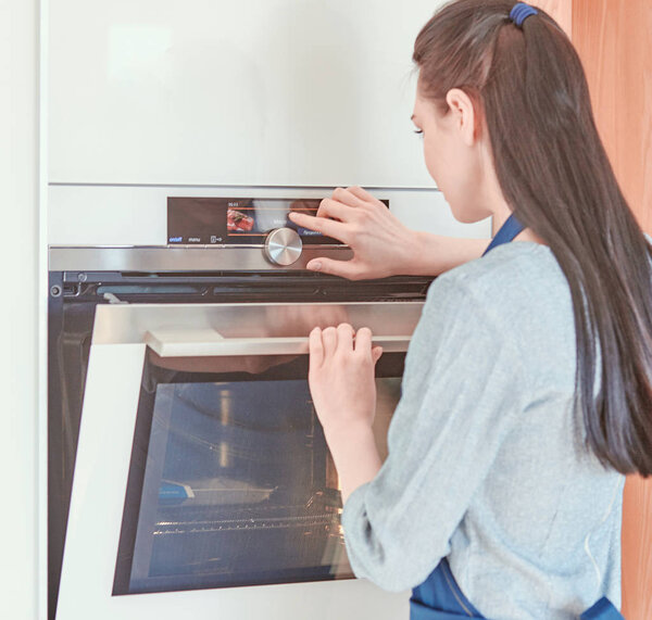 Beautiful woman in the kitchen, waiting with the front of the oven