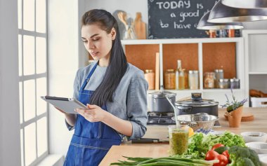 Mutlu kadın yemek tarifi arayan tablet mutfakta yemek yapıyor.