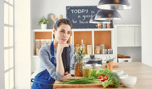 Szczęśliwa młoda kobieta w kuchni ze świeżych warzyw na stole — Zdjęcie stockowe