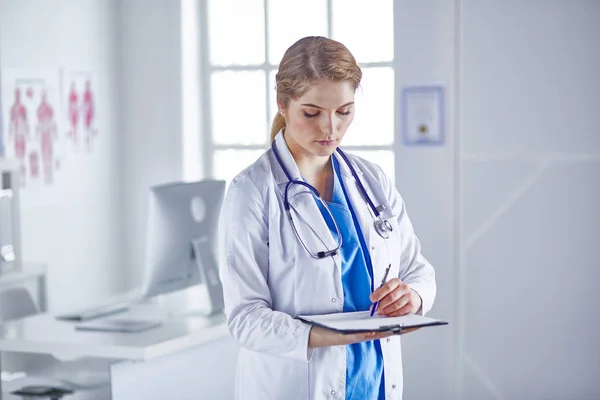 Jonge vrouw Doctor staat met Board met Klembord glimlachende — Stockfoto