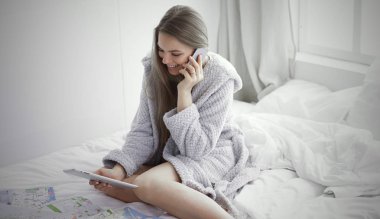 Telefon, tablet ve arama haritaları kullanarak yatakta mutlu genç kız