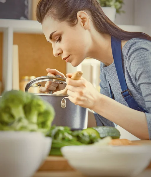 Bella ragazza sta assaggiando il cibo e sorridendo mentre cucina in kit — Foto Stock