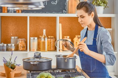 Güzel kız yemek tatma ve kit içinde pişirme sırasında gülümseyen