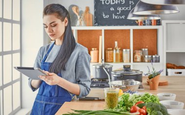 Mutlu kadın yemek tarifi arayan tablet mutfakta yemek yapıyor.
