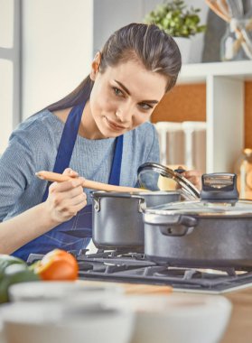 Güzel kız yemek tatma ve kit içinde pişirme sırasında gülümseyen