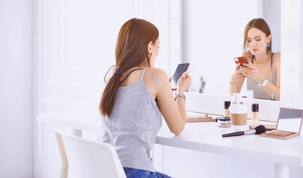 Amazing young woman doing her makeup in front of mirror. Portrait of beautiful girl near cosmetic table — Stock Photo, Image