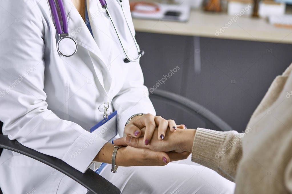 Woman doctor calms patient and holds hand