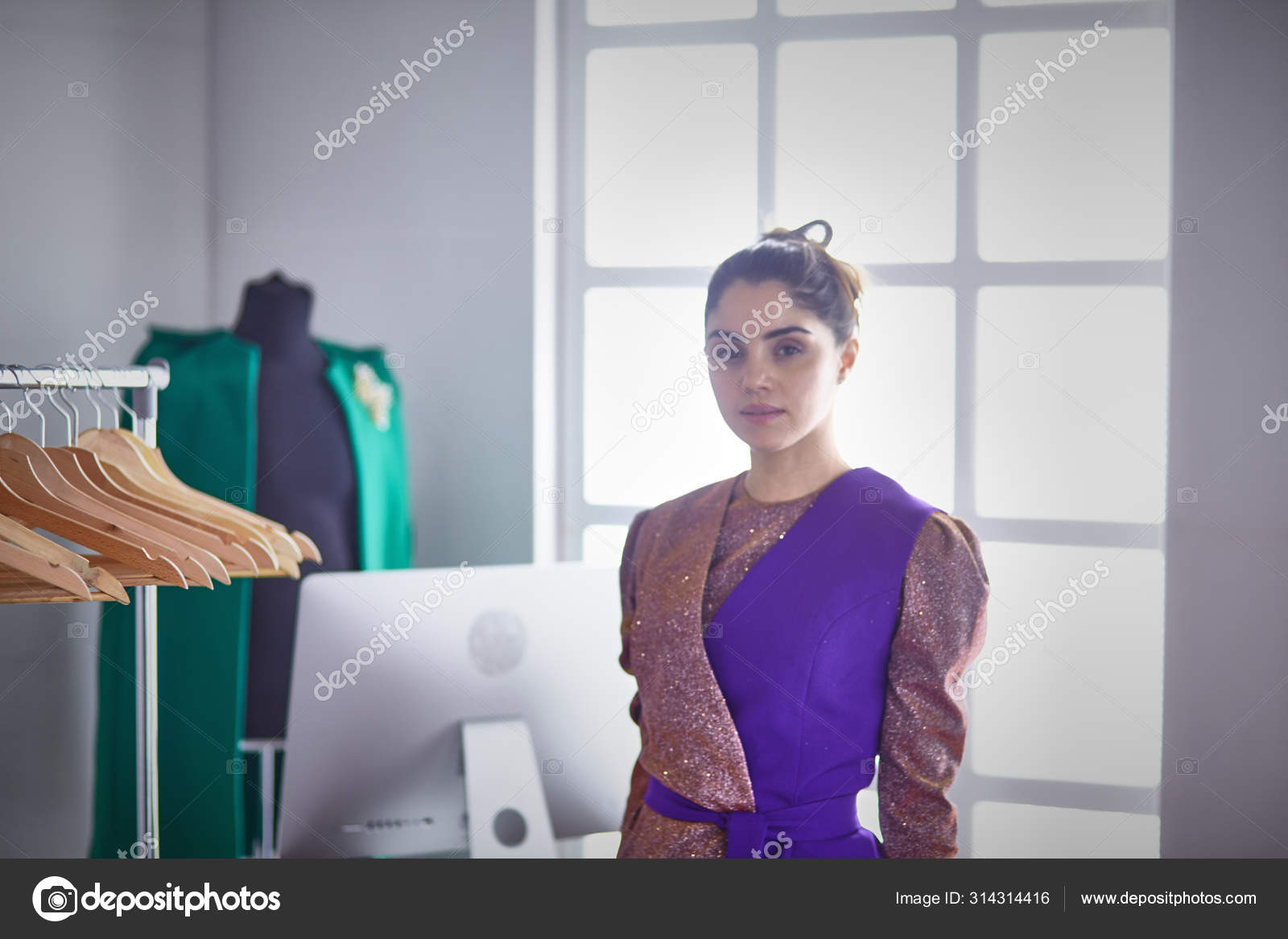 Beautiful young stylist holding clipboard near rack with designer ...