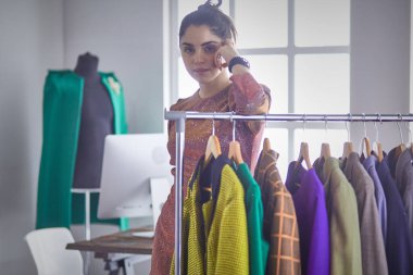 Pano raf giysi tasarımcısı ile yakınındaki beyaz arka plan üzerinde tutan güzel genç stilist