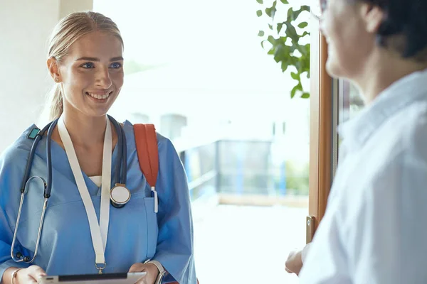 Eine junge Ärztin steht am Eingang zum Haus einer jungen Frau und ihrer kleinen Tochter — Stockfoto