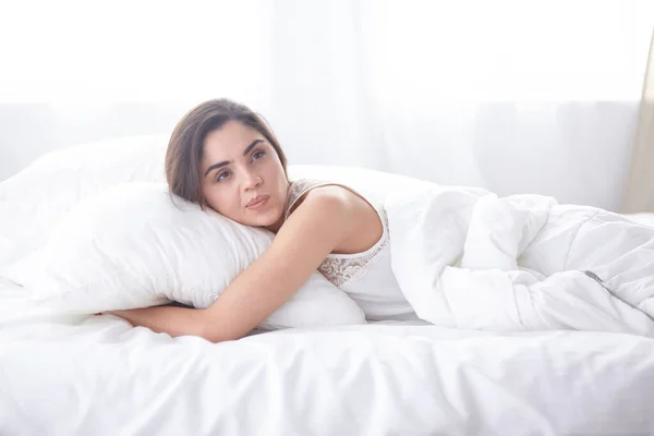 Прекрасная молодая женщина греется в постели по утрам. Красивое лицо модели выглядит сексуально в камере — стоковое фото