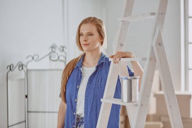 Beyaz tahta bir merdiven üzerinde güzel bir genç kadın. Odayı onarmaya hazırız. Kadın ev işi konsepti