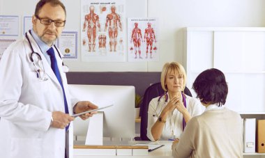 Orta yaşlı erkek doktor bir meslektaşının çalışmasına eşlik ediyor.