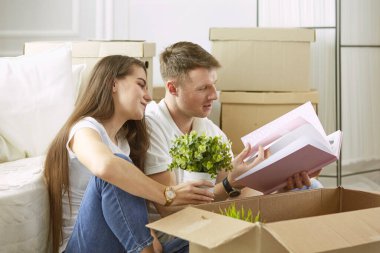 Birlikte dizüstü bilgisayara bakan mutlu bir çiftin portresi. Yeni evde oturuyorlar, kutularla çevrili.
