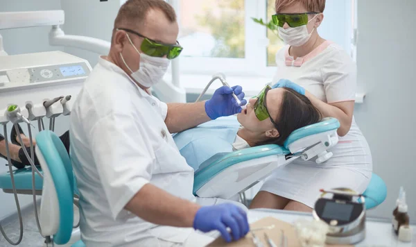 Médico dentista trata os dentes de uma bela jovem paciente. A rapariga na recepção do dentista. Médico dentista trata dente — Fotografia de Stock