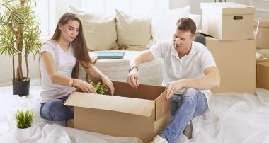 Birlikte dizüstü bilgisayara bakan mutlu bir çiftin portresi. Yeni evde oturuyorlar, kutularla çevrili.