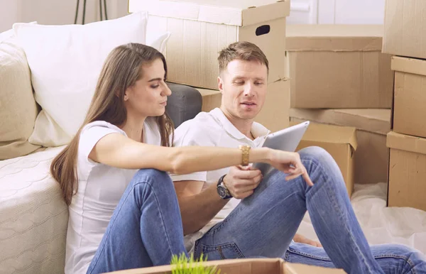 一对快乐的夫妇坐在新房子里，周围都是盒子，看着笔记本电脑的画像 — 图库照片