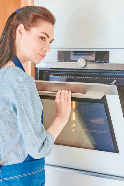 Beautiful woman in the kitchen, waiting with the front of the oven