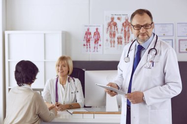 Orta yaşlı erkek doktor bir meslektaşının çalışmasına eşlik ediyor.