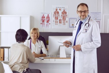 Orta yaşlı erkek doktor bir meslektaşının çalışmasına eşlik ediyor.