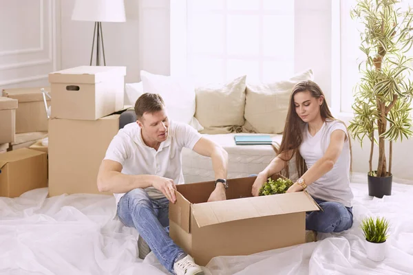 Retrato de casal feliz olhando para o computador portátil juntos sentados em casa nova, cercados de caixas — Fotografia de Stock