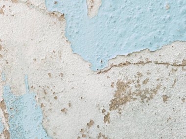 Yakın plan açık mavi boyalı duvar altında gri, pürüzlü beton olduğunu gösteren büyük, kabuk soyma bölümleri var. Eski boya dökülüyor ve açıkta kalan bölgelerin kenarlarında çatlaklar var.