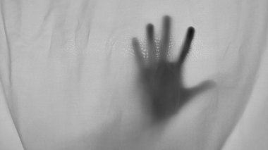 Siyah ve beyaz insan elinin gölgesi ince, beyaz, şeffaf kumaştan görülür. Kumaş buruşuk ve yumuşak dalgalar, dokulu arka plan oluşturuyor. Karanlık el, parmakları ayrık ve gizemli.
