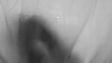 Siyah ve beyaz insan kafası ve elleri ince beyaz şeffaf kumaşın içinde gölgeler görüyordu. Kumaş buruşuk ve yumuşak dalgalar dokulu arka plan oluşturuyor. Gölge karanlık ve biraz bulanık