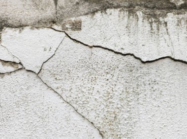 Görüntü çatlamış ve eskimiş beton yüzey. Çerçevenin ortasında yatay kıvrımlı büyük, siyah, sivri uçlu bir çatlak. Küçük çatlaklar dallanıp budaklanıyor.