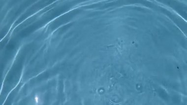 Gerçek zamanlı video 4K. Yakın plan açık mavi su yüzeyinde hafif dalgalanmalar var. Güneş ışığı sol alt köşedeki parlak yıldız patlamasını yansıtır. Doğayla ilgili arka planlar gevşeme saflığı