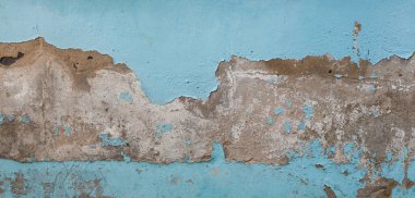 Horizontal dirty distressed cement wall with peeling light blue paint. Upper and lower parts of image show remnants chipped blue layer while center reveals the raw cracked gray concrete underneath