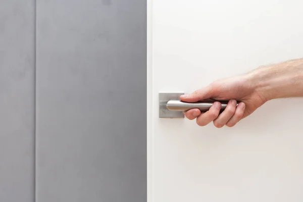 The man opens white door with metallic handle