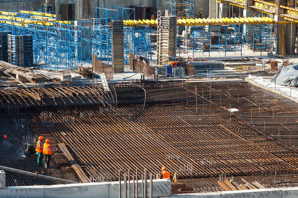 Construction of a large multi-storey commercial building. Builders work in overalls on the site pouring cement and concrete formwork, and tying the armature.