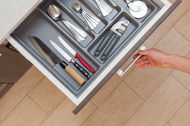 Yüksek açı üstten görünüm kırpılmış fotoğrafı kadın el farklı çatal kaşık, pizza bıçak, çatal ve malzeme ile kapı kolu tarafından mutfak çekmece açmak
