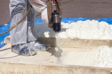 Teknisyen çoğul bileşen boya tabancası kullanarak köpük yalıtım püskürtme koruyucu beyaz üniforma giymiş. Çatı ve enerji tasarrufu için poliüretan köpük püskürtme