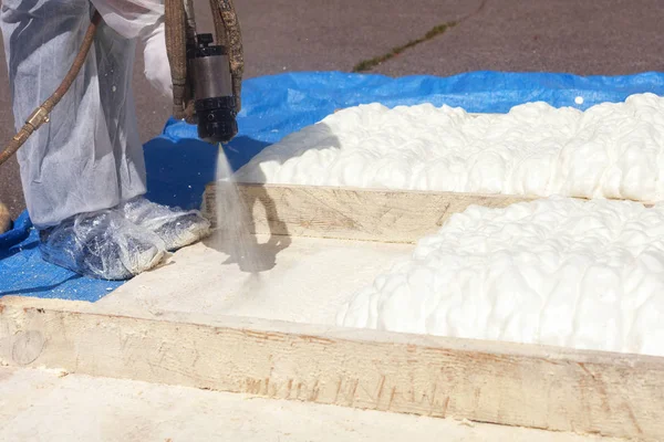Teknisyen çoğul bileşen boya tabancası kullanarak köpük yalıtım püskürtme koruyucu beyaz üniforma giymiş. Çatı ve enerji tasarrufu için poliüretan köpük püskürtme