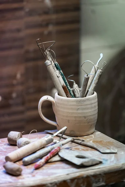 Vertical close up photo of tools for ceramics work stand in old vintage cup on table indoor workspace