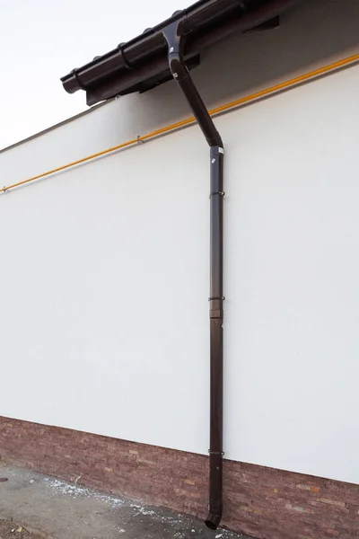 新しい快適さ家の白い壁に茶色の雨樋管の垂直写真 — ストック写真