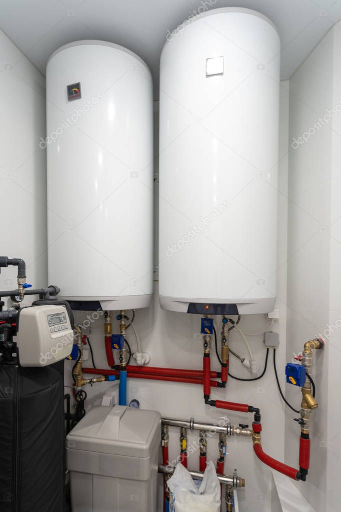 Vertical photo of central hydraulic boiler system with white heating water tanks and sensor panel element inside bright light room