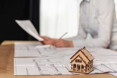 Kapatmak yukarıya ve seçici odak üstünde küçük bir ev. Onun resmi kıyafeti gömlekli konsantre Bayan hazırlamak belge Satılık düz veya Apartman Bina, o bulanık arka plan üzerinde kapalı ışık oda oturmak